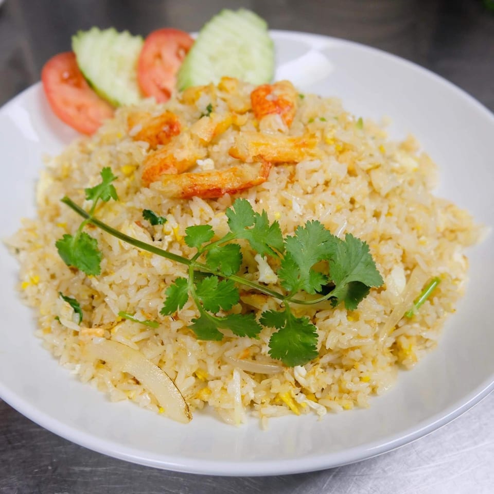 Thai fried rice with shrimp, egg, and vegetables, garnished with cilantro, cucumber, and tomato slices.